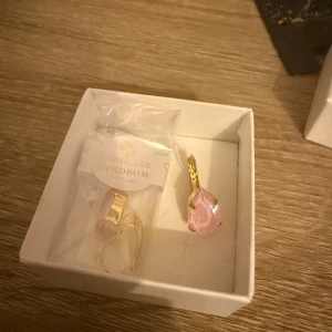 Caroline Svedbom örhängen rosa droppe färg soft pink - Snygga örhängen från Caroline Svedbom med droppformad rosa kristall och guldfärgade detaljer. Perfekt statement-piece med glittrig finish och elegant design. Kommer i originalask. Oanvänd och  färg soft pink. Köpt för 795, passar inte mina uttöjda öronsnibbar😢låda och emballage medföljer. 