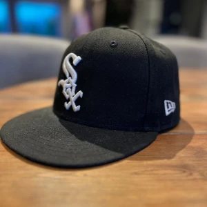 Svart New Era 59FIFTY White Sox keps - Säljer en svart New Era 59FIFTY keps med Chicago White Sox-logga broderad i vitt framtill. Klassisk flat brim och MLB-logga baktill. Kepsen är tillverkad i polyester och har en stilren look som passar perfekt till streetwear. Lite brunt där bak annars inget fel