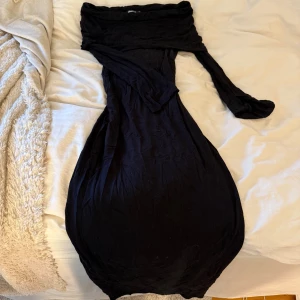 Svart långklänning från Gina Tricot - Svart långklänning från Gina Tricot med offshoulder-modell och lång ärmar med slits vid handen. Klänningen är figurnära och tillverkad i mjuk bomull, använd lite