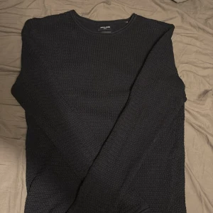 Svart stickad tröja Jack & Jones M - Säljer en svart stickad tröja från Jack & Jones i storlek M. Tröjan har en rund halsringning och långärmad design med snyggt strukturerat mönster i materialet. Perfekt för dig som gillar en stilren och enkel look.