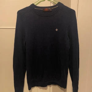 Mörkblå tröja i merinoull från Morris - Säljer en stilren mörkblå tröja från Morris i 100% merinoull. Tröjan har en liten broderad detalj på bröstet och långa ärmar. Perfekt för kyligare dagar.