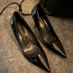 Svarta lackpumps med spetsig tå - Säljer ett par svarta pumps från YUANZHILIN i glansigt lackmaterial. Skorna har spetsig tå och smal hög klack som ger en elegant siluett. Perfekta för dig som vill sticka ut med en klassisk och stilren look.