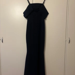 Marinblå glittrig långklänning - Säljer en marinblå långklänning med glittrigt tyg och smala axelband. Klänningen har en snygg offshoulder-detalj upptill och en elegant, figurnära passform som faller snyggt längs kroppen. Perfekt för dig som vill sticka ut med en stilren look.