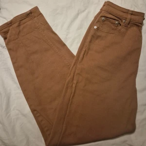 Bruna raka jeans med hög midja - Snygga bruna jeans med klassisk femficksdesign och raka ben. Byxorna har hög midja och silverfärgade nitar vid fickorna. Materialet är kraftig bomull med jeanskänsla, perfekt för en stilren och avslappnad look.