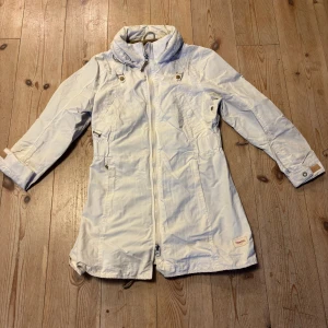 Vit parkajacka från Peak Performance - Snygg vit parkajacka från Peak Performance med hög krage och dragkedja framtill. Jackan har justerbara detaljer vid midjan och ärmarna samt praktiska fickor. Perfekt för dig som vill ha en stilren och funktionell jacka med längre passform.