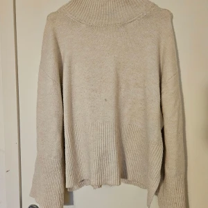 Vit polotröja från Gina Tricot - Mysig varmtvit polotröja från Gina Tricot i stickat material. Tröjan har bred ribbad kant nedtill och vid ärmslut, samt en hög polokrage. Lite nopprig samt liten fläck på framsidan som man ser på första bilden