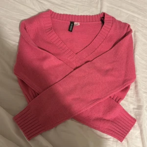 Rosa stickad v-ringad tröja - Superfin rosa stickad tröja från H&M med v-ringning och ribbade muddar vid ärmslut och nederkant. Perfekt för lager-på-lager och ger en poppig färg till din outfit. Klassisk passform och långärmad modell.