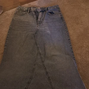 Lång jeanskjol från Gina Tricot - Säljer en snygg lång jeanskjol från Gina Tricot i klassisk blå denim. Kjolen har hög midja, bälteshällor, framfickor och en cool sömdetalj framtill. Perfekt för dig som gillar streetstyle och vill ha en chill vibe i garderoben.