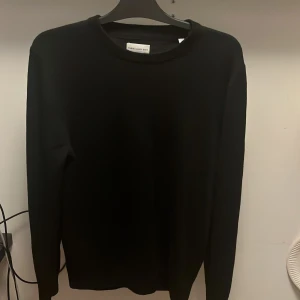 Svart merinoullströja These Glory Days - Säljer en stilren svart tröja från These Glory Days i mjuk och exklusiv merinoull. Tröjan har rund halsringning och långa ärmar, perfekt för lager-på-lager under kyliga dagar. Enkel design som funkar till allt och känns riktigt skön på.