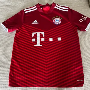 FC Bayern München matchtröja Adidas - Säljer en officiell FC Bayern München matchtröja från Adidas i röd färg med mörkröda chevronmönster. Tröjan har korta ärmar, vita detaljer och klubbmärke på bröstet. Tillverkad i lätt och ventilerande funktionsmaterial.