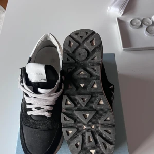 Philippe Model Trainers - Svarta sneakers från Philippe Model med vita detaljer och snörning. Ovandel i mocka och textil, vit logga på sidan och vit hälkappa. Det är storlek 39 IT passar 40. Sulan är vit med svarta inslag undertill och har ett sportigt, trendigt utseende. Perfekta för en stilren och Grisch look. Perfekta skor till vintern