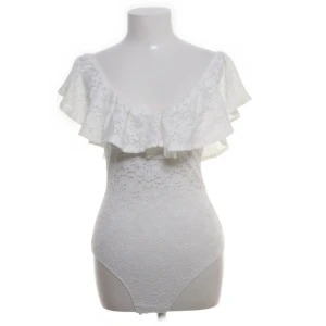 Vit volang body från Oysho - Superfin vit body från Oysho med romantiska volanger över axlarna och v-ringad hals. Hela bodyn är täckt av spetsliknande mönster som ger en söt och somrig känsla💗💗