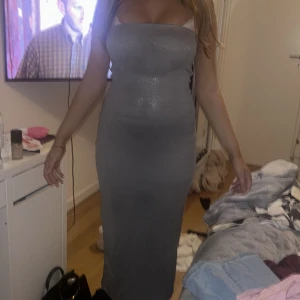 Grå glittrig långklänning - Säljer en snygg grå långklänning med glittrigt tyg och figurnära passform. Klänningen är axelbandslös och har en slits bak för extra rörelsefrihet. Perfekt för dig som vill sticka ut med en elegant och modern look. Lappen e it kvar så vet ej märket.