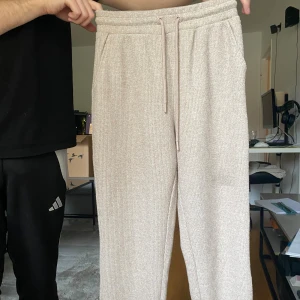 Rosa/Beige ribbade mjukisbyxor med snörning - Säljer ett par rosa/beige ribbade mjukisbyxor med snörning i midjan. Byxorna har en relaxed fit och är perfekta för chill dagar. Mjukt material och elastisk midja för extra komfort.