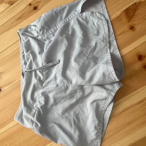 Nike träningsshorts - Nike Dri-Fit shorts i ljusgrått, perfekta för träning. De har en loose passform, elastisk midja med snörning och är tillverkade i ett lätt syntetmaterial som andas. 
