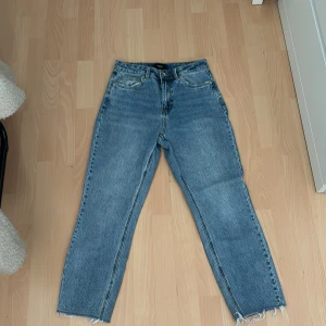 Blå raka jeans från Vero Moda - Säljer ett par klassiska blå jeans från Vero Moda med raka ben och råa, fransiga benslut. Jeansen har hög midja, fem fickor och stängs med dragkedja och knapp. Perfekta till sneakers eller boots för en chill look.
