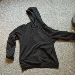 Svart hoodie med tryck på ryggen - Svart hoodie med stor huva och snörning, samt en rymlig magficka framtill. På ryggen finns pop smoke! Tröjan har långa ärmar och är gjord i mjukt bomullsmaterial, perfekt för en chill och urban stil.