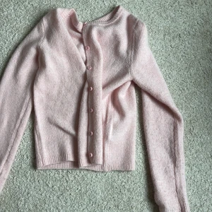 Ljusrosa kofta från 157, storlek S - Supermjuk ljusrosa kofta från 157 i stickat material. Koftan har rund halsringning, långa ärmar och matchande rosa knappar framtill. Perfekt för lager-på-lager och ger en söt vibe till din outfit.