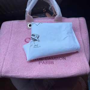 Rosa stor handväska  - Stor och rymlig shoppingväska i ljusrosa tyg med text på framsidan. Väskan har två handtag, silverfärgade detaljer och en kedja inuti. Perfekt för dig som vill ha en trendig och snygg väska med plats för allt.