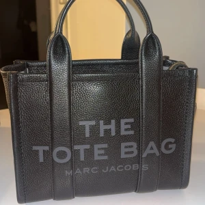 Svart The Tote Bag från Marc Jacobs - Säljer min Marc Jacobs Tote Bag i svart äkta läder då jag tyvärr råkat köpa fel storlek. Väskan är i princip helt ny, använd endast 2 gånger. Inga defekter, repor eller märken, den ser ut som ny.  100% äkta autenticitetspapper och kort medföljer  Material: 100% ko-läder Färg: Svart  Modell: The Tote Bag (medium) 🖤