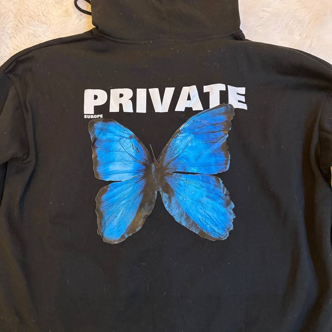 Svart hoodie med blå fjäril och text