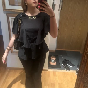 Svart volangblus med vida ärmar - Säljer en svart blus med snygga volangdetaljer framtill och på sidorna. Blusen har vida, korta ärmar och en lös passform.Perfekt nu till hösten🩷