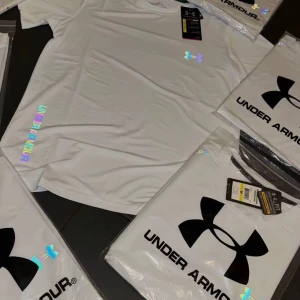 Vit Under Armour set reflective size L - Fräsch vit t-shirt från Under Armour med holografiskt logotryck på bröstet och längs sidan. Skön passform och tillverkad i lätt polyester som andas, perfekt för träning. Klassisk rund hals och korta ärmar. Snygg sportig vibe med coola detaljer.