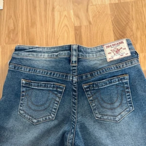 True Religion Bobbi Baggy jeans blå - Säljer ett par blåa True Religion Bobbi Baggy jeans med klassiska bakfickor och ljus tvätt. Jeansen har en avslappnad baggy passform och är tillverkade i jeansmaterial. Märkespatch bak i midjan och coola sömdetaljer på fickorna.