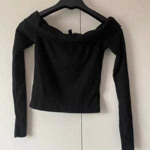 Svart offshoulder topp H&M XS - Säljer en svart ribbad offshoulder topp från H&M i storlek XS. Toppen har långa ärmar och en bred, nedvikt krage som ger en snygg offshoulder-look. Perfekt att styla med jeans eller kjol för en trendig outfit.