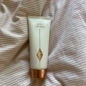 Goddess Skin Clay Mask Charlotte Tilbury - Goddess Skin Clay Mask från Charlotte Tilbury i en vit tub med guldig kork. Masken är på 75 ml och ger en mjuk, återfuktad känsla och jämnar ut hudtonen. Perfekt för dig som vill ha en lyxig ansiktsmask som ger glow och minimerar porer. Har ett par defekter på framsidan. Har använt en gång. Nypris: 575kr