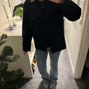 Svart kappa från Gina Tricot - Stilren svart skepparkavaj från Gina Tricot med bred krage och knäppning framtill. Jackan har en rak passform och är tillverkad i ett ullblandat material som passar perfekt till kyligare dagar. Enkel att matcha med jeans eller kjol för en snygg look. Storlek 158/164