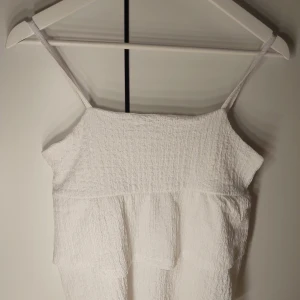 Vit linnetopp från Kappahl - Supersöt vit linnetopp från Kappahl med smala axelband och volangdetalj framtill. Toppen har en lätt skrynklig struktur i tyget och är perfekt för varma dagar. Enkel och stilren design som är lätt att matcha med allt.