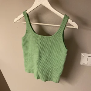 Grön ribbad linnetopp från FB Sister knitwear - Superfin ljusgrön ribbad linnetopp från FB Sister knitwear. Croppad modell med breda axelband och rundad halsringning. Stickad känsla i materialmix av viskos, polyester och polyamid.