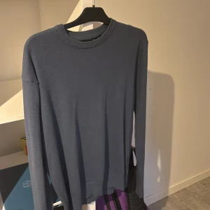 Mörkblå stickad tröja med rund hals - En stilren mörkblå stickad tröja med rund halsringning och långa ärmar. Tröjan har en enkel design utan mönster och är perfekt för lager-på-lager. Mjuk och skön känsla, passar till jeans eller chinos.