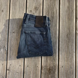 Replay Anbass jeans i mörkblå denim - Säljer ett par Replay Anbass jeans i mörkblå tvättad denim. Klassisk femficksmodell med snygga detaljer och logga på bakfickan. Jeansen har smal passform och raka ben, perfekt för dig som gillar en stilren look. Materialet är mjukt och stretchigt för extra komfort.