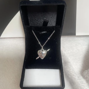 Silverhalsband med  detaljerat hjärthänge - Snyggt halsband i silverfärg med ett coolt hjärthänge som har en pil genom sig. Kedjan är tunn och smidig, perfekt för att ge din outfit lite edge. Hjärtat har en blank finish och känns både trendigt och tidlöst. Rostfri