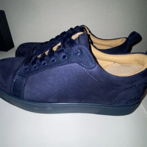 Louboutins - Snygga mörkblå sneakers från Christian Louboutin i mocka med klassisk röd sula. Skorna har rund tå, snörning och beige innersida. Perfekta för dig som vill ha en stilren och lyxig look med en ikonisk touch. Var inte rädd att skriva 
