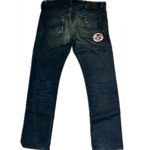 Diesel jeans - Snygga mörkblå jeans med coola patchar framtill och baktill samt slitna detaljer för en edgy look. Jeansen har raka ben och klassisk femficksdesign. Perfekta för dig som vill sticka ut med en unik streetstyle.