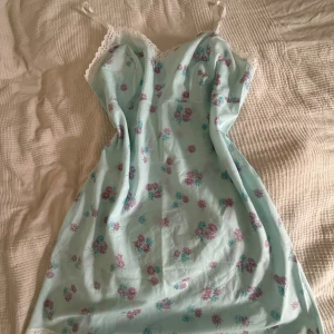 Ljusblå blommig sommarklänning med spets - Söt ljusblå klänning med rosa och blå blommor, tunna axelband och vit spetskant upptill och nertill. Mycket fint skick- uppskattad storlek S/M