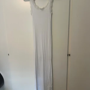 Vit långklänning med spetsdetaljer - En vit tajt långklänning med smala axelband och spetsdetaljer vid halsringningen från Pure Friday i storlek XS säljes för 200kr. 