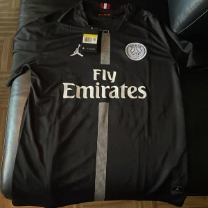 PSG Neymar Jr svart matchtröja Jordan S - Svart PSG fotbollströja i samarbete med Jordan, Neymar Jr 10 på ryggen. Klassisk passform, kortärmad och tillverkad i lätt, ventilerande polyester. Vit logga, emblem och sponsortryck framtill, samt en smal rand i mitten. Röd och vit detalj i nacken.