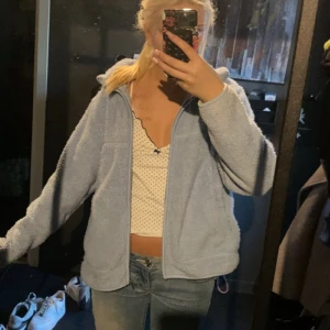 Ljusblå teddyjacka med dragkedja - Mysig ljusblå teddyjacka med dragkedja framtill och huva. Jackan har en avslappnad passform och är tillverkad i fluffigt fleece-material som känns supergosigt. Perfekt för kyliga dagar när du vill vara både bekväm och snygg.