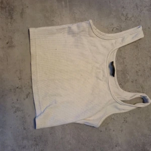 Vit ribbad linnetopp - Säljer en enkel och fräsch vit linnetopp med ribbad struktur. Modellen är croppad och har breda axelband, perfekt för att styla med jeans eller shorts. Materialet känns mjukt och stretchigt, vilket gör den skön att bära under varma dagar. Denna är från shein. Priset är lågt pågrund av att jag fick tröjan k dåligt skick av förra jag köpte den av.