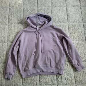 Ljuslila hoodie - En stilren ljuslila hoodie med huva och snörning. Tröjan har ribbade muddar vid ärmslut och nederkant, samt en relaxed passform. Perfekt för dig som gillar en enkel men snygg look. Materialet känns mjukt och skönt, troligtvis bomull eller bomullsblandning.