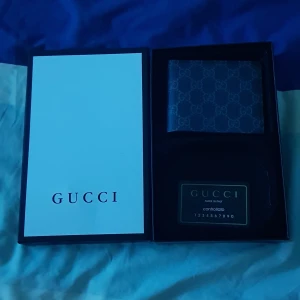 Svart plånbok från Gucci med GG-mönster - Snygg svart plånbok från Gucci med klassiskt GG-mönster över hela ytan. Plånboken är tillverkad i skinn och har flera fack för kort samt ett fönster för ID. Kommer i originalask med kontrollkort. Perfekt för dig som gillar stilrena accessoarer.