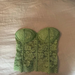 Grön spetskorsett med blommönster - Säljer en ljusgrön korsett med blommig spets och snygga sömmar som framhäver formen. Toppen är axelbandslös och har en dragkedja i ryggen för enkel på- och avtagning. Perfekt för dig som vill ha en statement piece i garderoben!