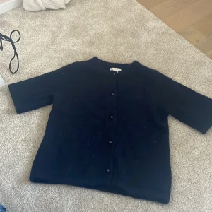 Svart kofta från Gina Tricot - Mysig svart kofta från Gina Tricot med rund halsringning och knappar framtill. Koftan har halvlånga ärmar och är stickad i ett fluffigt material. Den är helt ny aldrig använd, pris kan diskuteras 