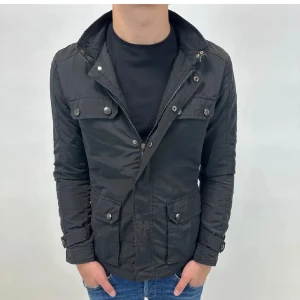 Svart field jacket - Snygg svart vindjacka med fyra framfickor och detaljerade knappar. Jackan har dragkedja och tryckknappar framtill samt justerbara ärmslut. Perfekt för dig som gillar en stilren och funktionell look.