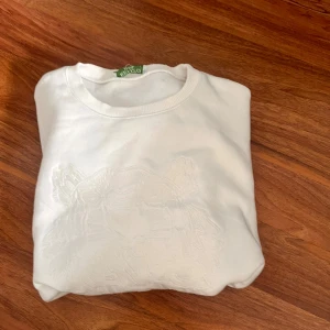 Vit sweatshirt från Kenzo med broderad tiger - Säljer en vit sweatshirt från Kenzo med ikonisk broderad tiger på bröstet. Tröjan har rund hals, ribbade muddar och är tillverkad i mjuk bomull. Perfekt för dig som gillar stilrena och snygga designer med en twist.