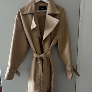 Beige trenchcoat från Bik Bok - Stilren beige trenchcoat från Bik Bok i storlek S. Jackan har klassisk krage, bälte i midjan och spännen vid ärmsluten. Tillverkad i ett mjukt bomullsmaterial som ger en snygg och clean look. Perfekt för dig som vill ha en tidlös och trendig jacka. Köpte jackan för 900 kr och den är knappt använd✨